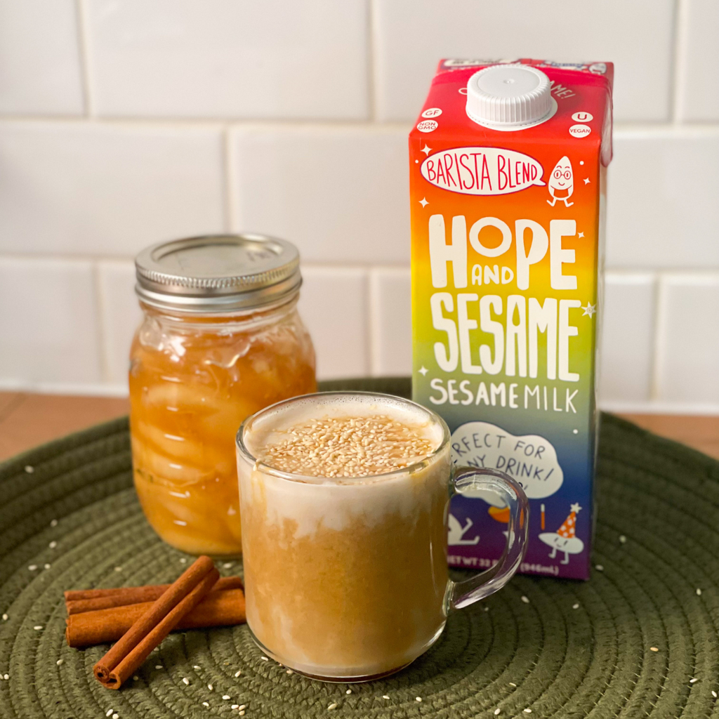 Glass mug of Hope and Sesame® Apple Pie Latte with cinnamon sticks and a carton of Barista Blend 