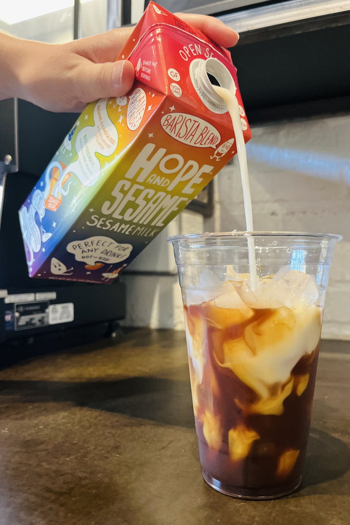 Dairy alternative Hope and Sesame Sesamemilk, carton of Barista Blend shown being poured into a cup of iced coffee