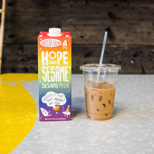 Dairy alternative Hope and Sesame Sesamemilk, Barista Blend carton on counter with iced coffee