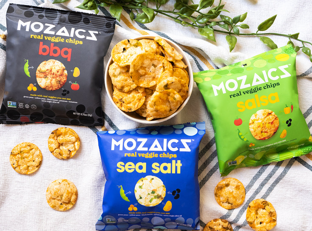 Healthy snack chips Mozaics Chips, packet of all three flavors in Sea Salt, BBQ and Salsa on a table cloth with a bowl of Mozaics chips